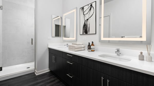 Dog-Friendly Apartments in Uptown Chicago, IL - Eight Eleven Uptown - Bathroom with Double Vanity,Quartz Countertop, Dark Colored Cabinets, Mirrors, Shower with Glass Door, and Wood-Plank Flooring.