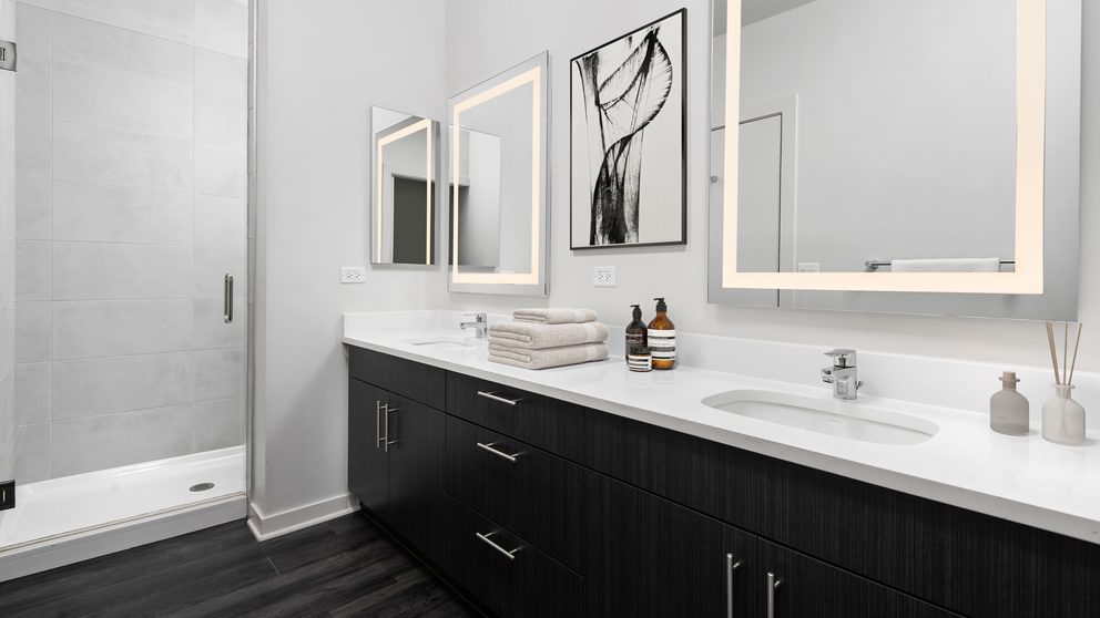 Dog-Friendly Apartments in Uptown Chicago, IL - Eight Eleven Uptown - Bathroom with Double Vanity,Quartz Countertop, Dark Colored Cabinets, Mirrors, Shower with Glass Door, and Wood-Plank Flooring.