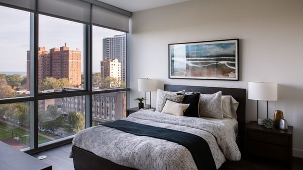Uptown Chicago, IL, Pet-Friendly Apartments - Eight Eleven Uptown - Bedroom with Floor-to-CeilingWindows, Large Bed, Nightstands with Lamps, and Wood-Plank Flooring.