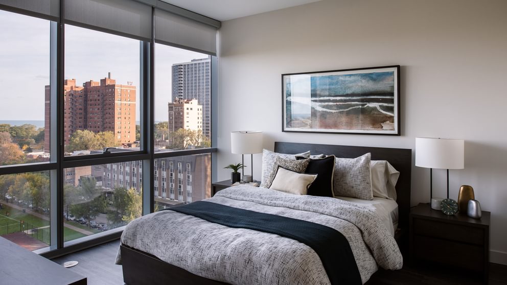 Uptown Chicago, IL, Pet-Friendly Apartments - Eight Eleven Uptown - Bedroom with Floor-to-CeilingWindows, Large Bed, Nightstands with Lamps, and Wood-Plank Flooring.